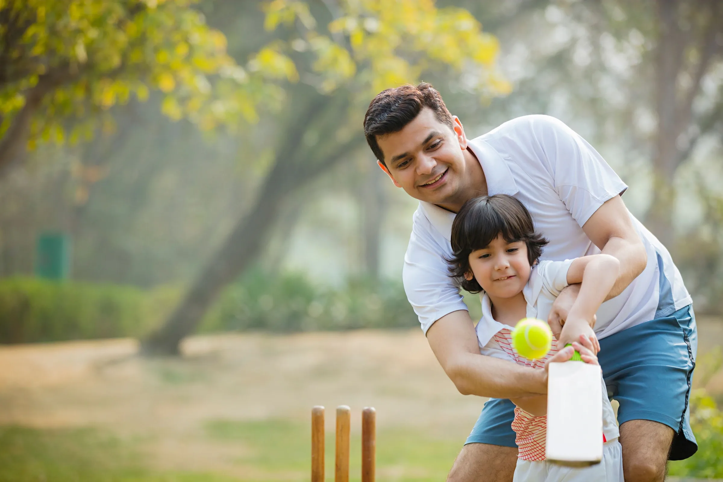 A father teaching his son to play cricket on a green lawn